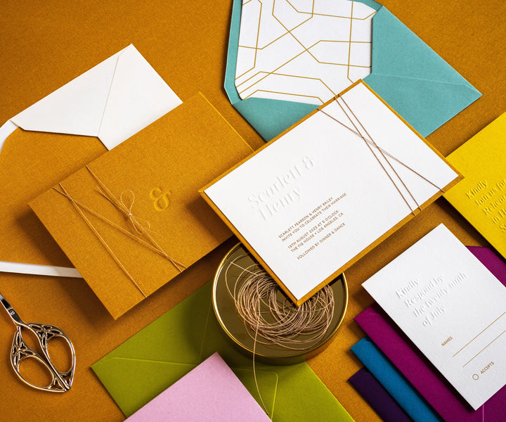 Angled top view of colourful letterpress wedding invitation set and envelopes