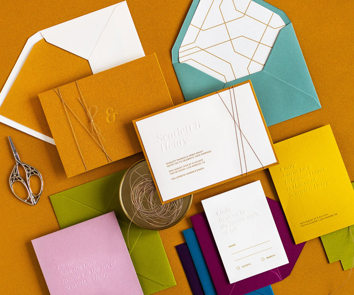 Angled top view of colourful letterpress wedding invitation set and envelopes